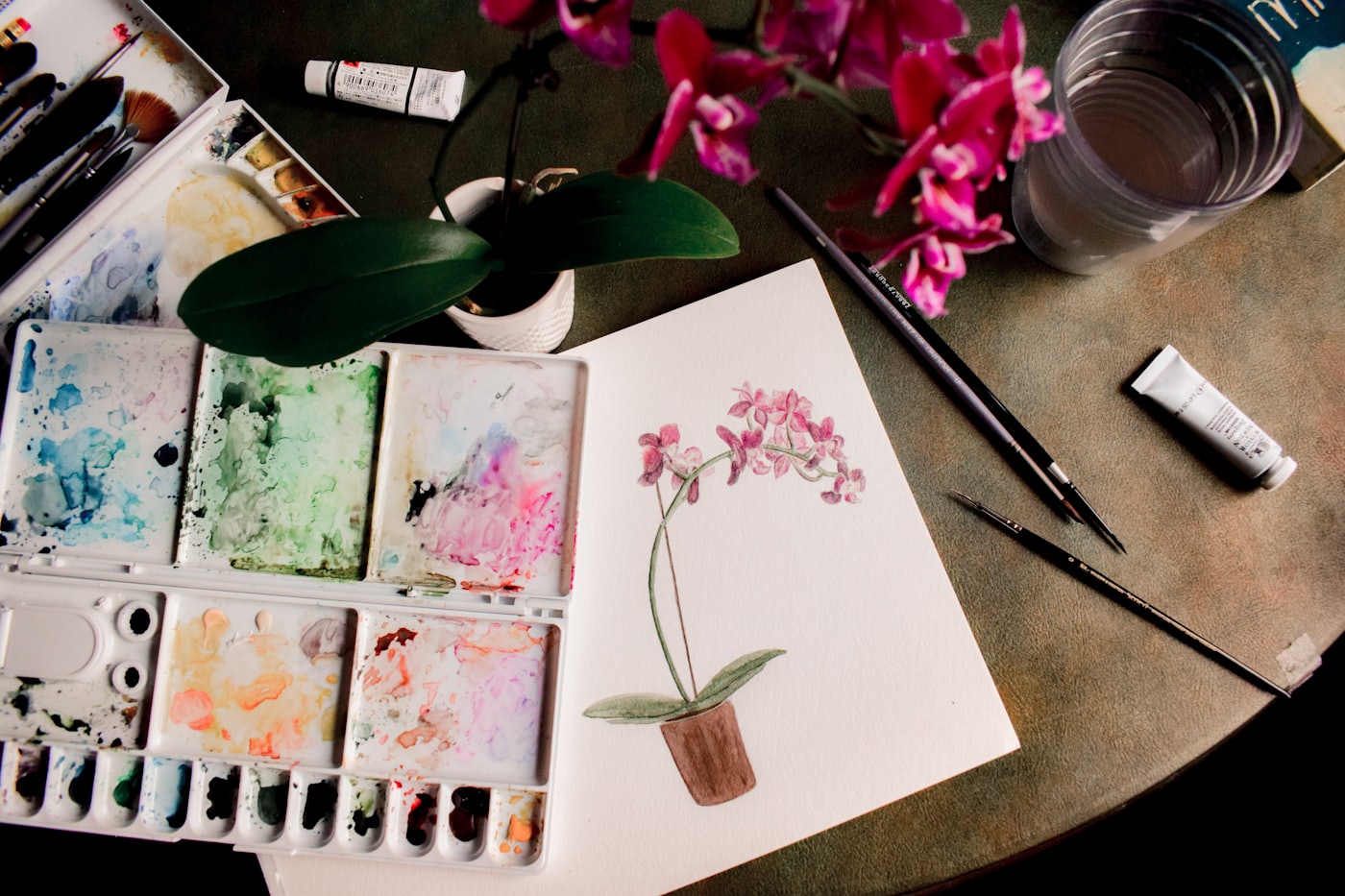 A watercolour orchid being painted, with palette and brushes